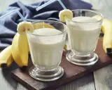 Dwa bananowe koktajle proteinowe w szklankach z rurkami i plasterkami banana. Idealne, gdy pić shake proteinowy po treningu.