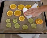 En hand torkar apelsinskivor på en plåt med bakplåtspapper. Citrusfrukter förbereds för att torka.