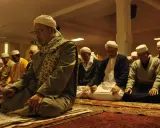 Männer in weißen Turbanten und traditioneller Kleidung knien auf Gebetsteppichen und verrichten das Taraweeh-Gebet.