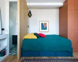 Une chambre cabine cosy avec un lit bleu canard, des coussins colorés et une armoire ocre. Un paravent en bois sépare l'espace nuit de la salle de bain.
