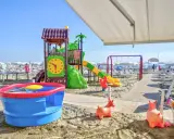 Area giochi su sabbia con scivolo, altalena e giochi d'acqua, un vero lido per bambini.