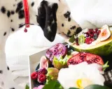 Dalmatyńczyk wącha owoce, zastanawiając się, jakich owoców nie może jeść pies. Na tacy figi, kiwi, maliny, granaty i papaja.