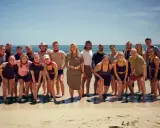 En grupp glada robinson deltagare poserar på en strand med havet i bakgrunden.