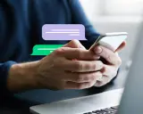 Hände halten ein Smartphone, über dem Chat-Blasen schweben. Vorsicht vor Smishing, der Betrugsmasche per SMS.