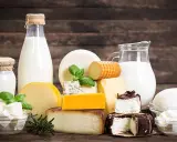 Milchprodukte wie Käse und Milch, die Laktose enthalten, sind auf einem Holztisch arrangiert.