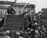 Lenin spricht von einer improvisierten Bühne zu einer großen Menschenmenge. Die Szene wirkt wie eine "revolution von oben", die das Volk mobilisiert.