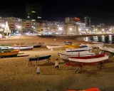 Boote am Strand bei Nacht, beleuchtete Stadt und Weihnachtsbaum. Selbst im Spanien Winter ist die Temperatur angenehm für einen Spaziergang.