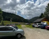Parking z samochodami przy górskim schronisku, w tle las i chmury.