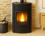 Poêle à granulés sans ventilation, flammes vives dans la vitre, à côté d'un seau de granulés et d'un meuble en bois.