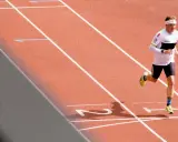 Läufer mit Stirnband und Laufbekleidung auf einer roten Laufbahn, der sich auf sein polarisiertes Training konzentriert.