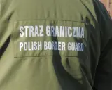 Fragment zielonego munduru Straży Granicznej z białym napisem "STRAŻ GRANICZNA POLISH BORDER GUARD".