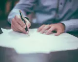 Dłoń pisze piórem na papierze, przygotowując list formalny angielski matura.