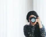 Kobieta z aparatem Canon, skupiona na kadrze. Rozwija swój biznes fotograficzny, łapiąc chwile.