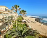 Fuerteventura kiedy wieje, palmy kołyszą się nad piaszczystą plażą i oceanem. Hotel z tarasami i widokiem na fale.