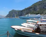 Barche in attesa al porto, con la maestosa isola di Capri sullo sfondo. Un traghetto Caremar attende passeggeri da Napoli.
