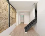 Interior moderno con pared de piedra rústica, escaleras oscuras y suelo de madera clara. Un ejemplo de cómo hacer una casa sostenible combinando lo antiguo y lo nuevo.