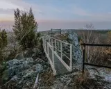 Mostek na skalnym ostańcu na Jurze Krakowskiej. W oddali las i niebo o zmierzchu.