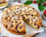 Saftiger Kirschkuchen mit frischen Kirschen, bestäubt mit Puderzucker. Ein Stück wird gerade herausgeschnitten.