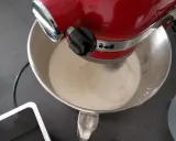 Un robot pâtissier rouge mélange une crème onctueuse, étape clé pour réussir une pâte à bombe aérienne.