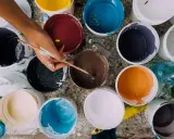 Ręka artysty miesza farby w wiaderkach. Widać różne kolory, ale też potencjalne wady farby ceramicznej, jak nierównomierne rozprowadzenie.