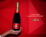 Eine Hand hält eine Flasche Piper-Heidsieck Champagner vor rotem, geometrischem Hintergrund.