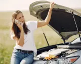 Mujer llama por teléfono con el capó abierto, preocupada por qué pasa si el coche se queda sin aceite.
