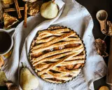 Tarte d'Halloween en forme de momie, avec des yeux globuleux et une garniture aux fruits. Autour, des feuilles d'automne, des poires et des épices.