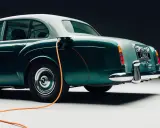 Clásico Bentley con cable de carga naranja conectado. Un ejemplo de retrofit que es la electrificación de vehículos antiguos.