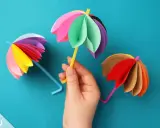 Bunte Papier-Regenschirme, tolle bastelideen einfach und schnell für Kinder. Ein gelber Schirm wird von einer Hand gehalten.