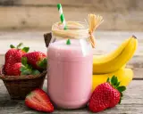 Delicioso batido de fresa y plátano, con fresas frescas y plátanos amarillos de fondo.