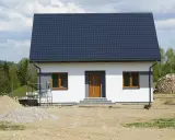 Nowy dom z ciemnym dachem i białymi ścianami, gotowy na zawiadomienie o zakończeniu budowy. Wokół plac budowy z piaskiem i drewnem.