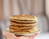 Pile de pancakes dorés à la farine de sarrasin, servis sur une assiette blanche tenue par une main.