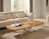 Mesa centro elevable 120x70 de madera clara, con un libro abierto y taza de café, junto a un sofá beige en un salón luminoso.