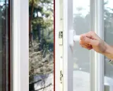 Mano girando la maniglia de unas ventanas pvc plegables, abriendo la vista a un paisaje nevado.