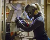 Kobieta w masce spawalniczej wykonuje spawanie w domu. Precyzyjnie łączy metalowe elementy, tworząc coś nowego.