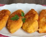 Cuatro pechugas villaroy doradas y crujientes, servidas en un plato blanco con una ramita de perejil.