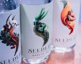 Drei Flaschen Seedlip alkoholfreien Gin mit kunstvollen Etiketten, die fantasievolle Tiere und Pflanzen zeigen.