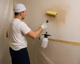 Hombre con rodillo y pulverizador aplica producto para como quitar gotele de la pared.