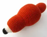 Un adorable zorro amigurumi de lana naranja, con detalles blancos y negros en el hocico, listo para jugar.