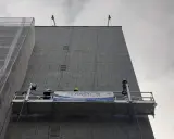 Dos trabajadores en andamios suspendidos realizan labores en la fachada de un edificio.