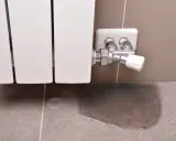 Un radiador que gotea deja un charco de agua en el suelo de baldosas, señal de un problema de fontanería.
