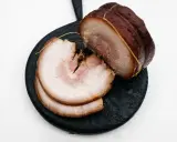 Pokrojony boczek chashu, z widocznymi warstwami mięsa i tłuszczu, ułożony na ciemnej desce.
