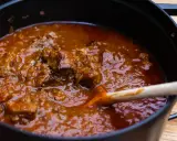 Ein dampfender Topf mit zartem Wiener Saftgulasch, das mit einer Holzschaufel umgerührt wird.