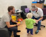 En pappa och ett barn får vaccin av en sjuksköterska. Barnet verkar lite oroligt, men sjuksköterskan är lugn och trygg. Det är en fin stund av vaccin italien.