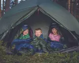 Tre glada barn myser i sina sovsäckar i ett tält. En perfekt tältsäng barn för äventyr i skogen.