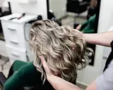 Profesjonalne usługi fryzjerskie: stylista układa falowane, blond włosy klientki w salonie.