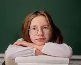 Dziewczynka w okularach opiera głowę na stosie książek. Zastanawia się, do kiedy można pobierać zasiłek rodzinny.