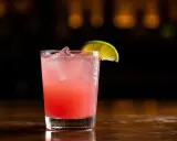 En rosa tequila drink med is och en limeklyfta på en mörk bakgrund.