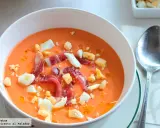 Un cuenco blanco con salmorejo cordobés, coronado con huevo duro picado y taquitos de jamón serrano.