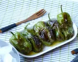 Délicieux **pieds de poivrons** verts, grillés et saupoudrés de gros sel, servis dans une assiette blanche avec une fourchette en bois.